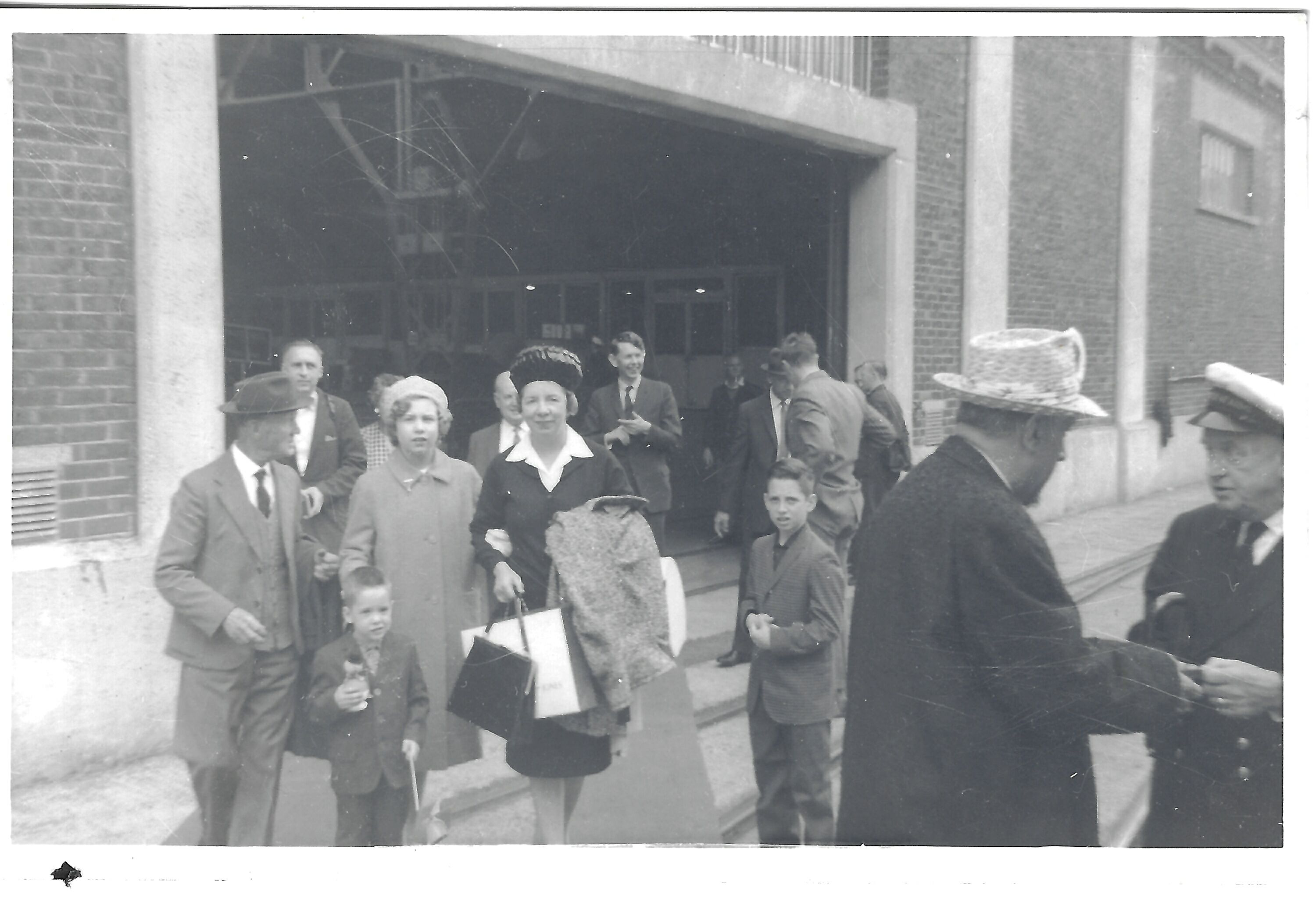 A group outside a large building, apparently including some travelers in the nearby ship-deck photograph. The place, date, and voyage direction remain unverified.
