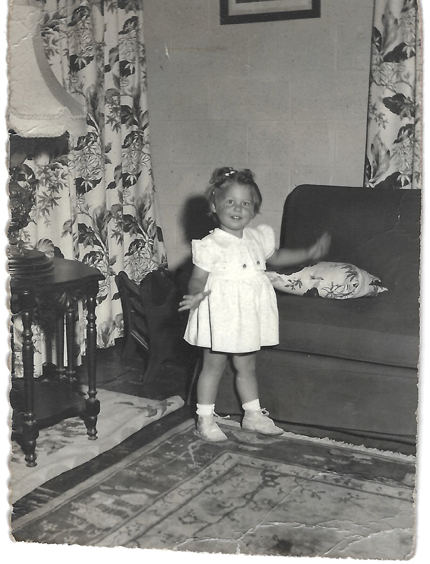 Young Betty standing beside a sofa