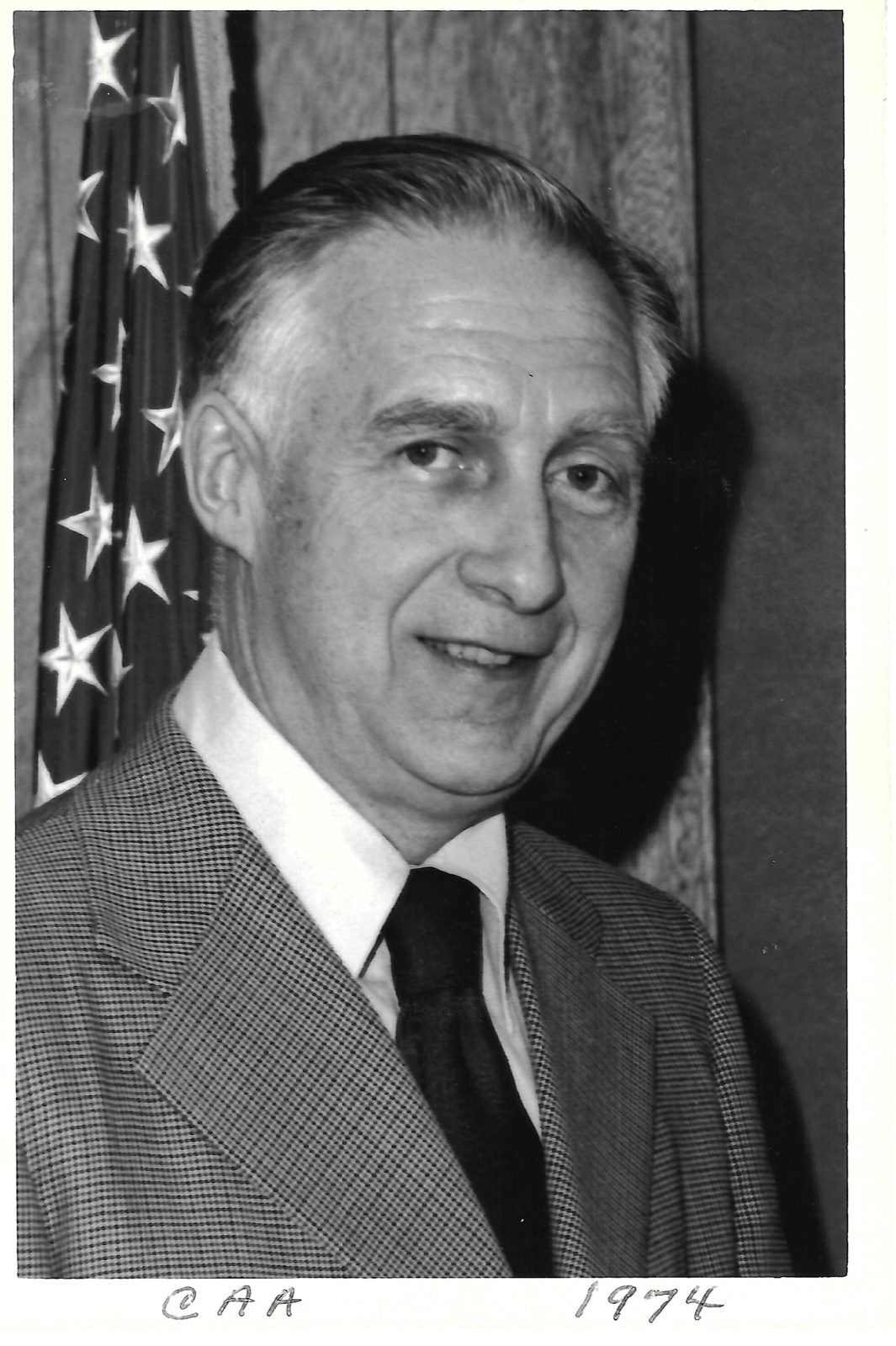 Jack Newman in front of an American flag, labeled CAA, February 1974.