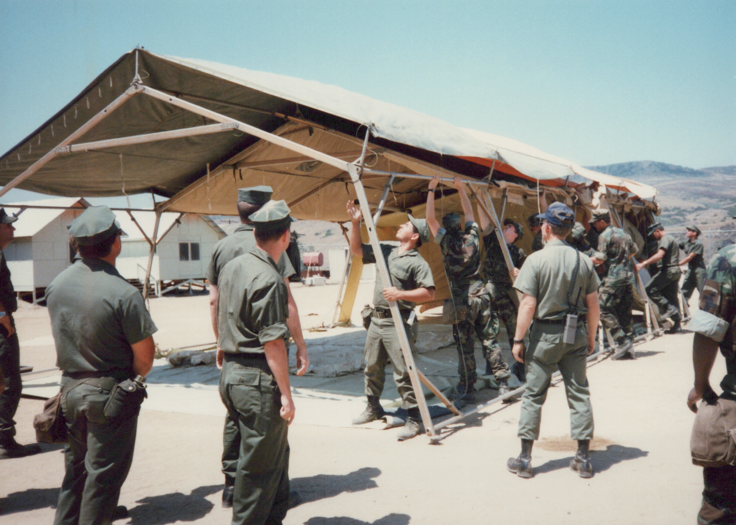 Fleet Hospital 007: People work around the frame of a large open shelter.