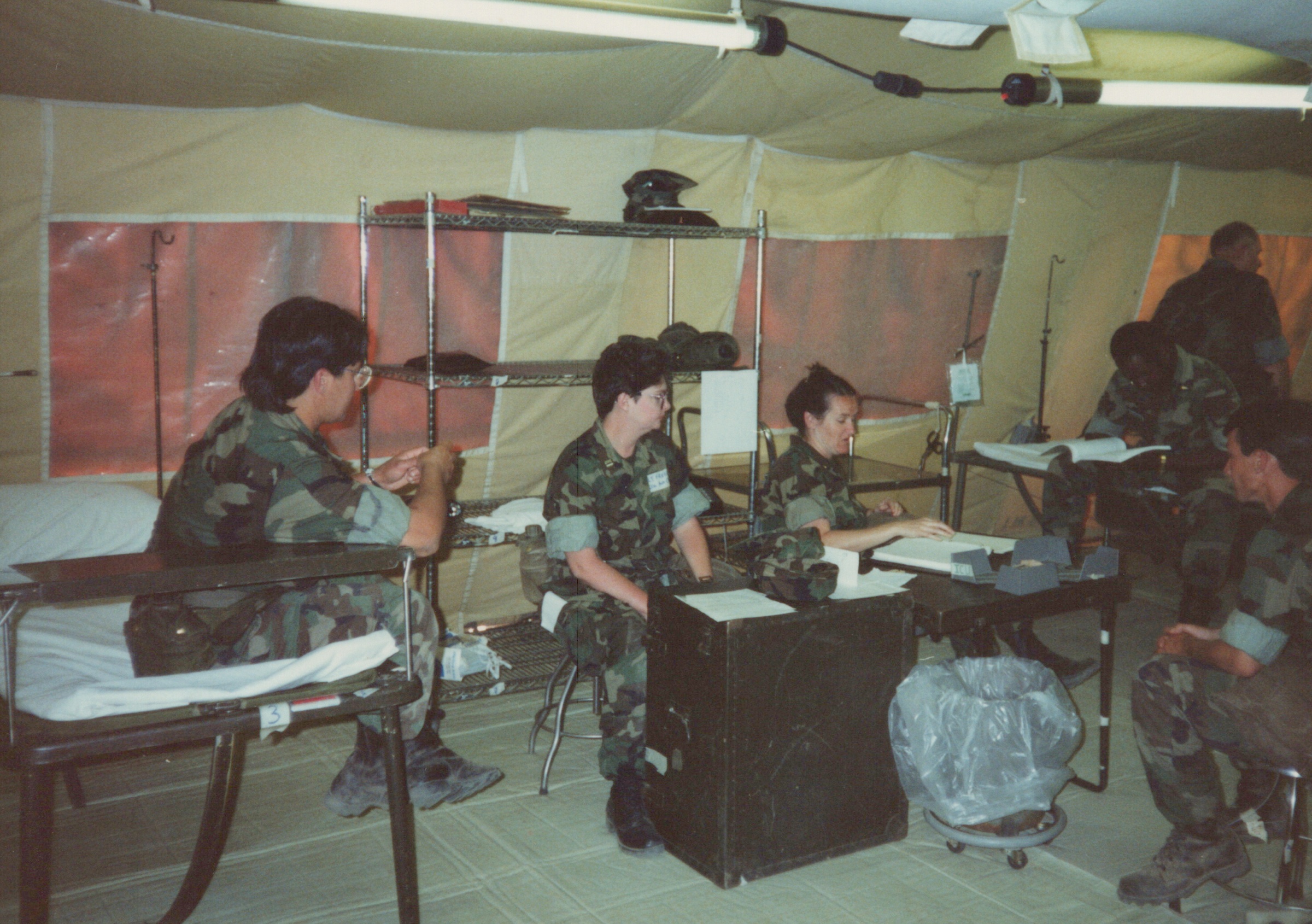 Fleet Hospital 007: Uniformed personnel work at tables inside a tent.