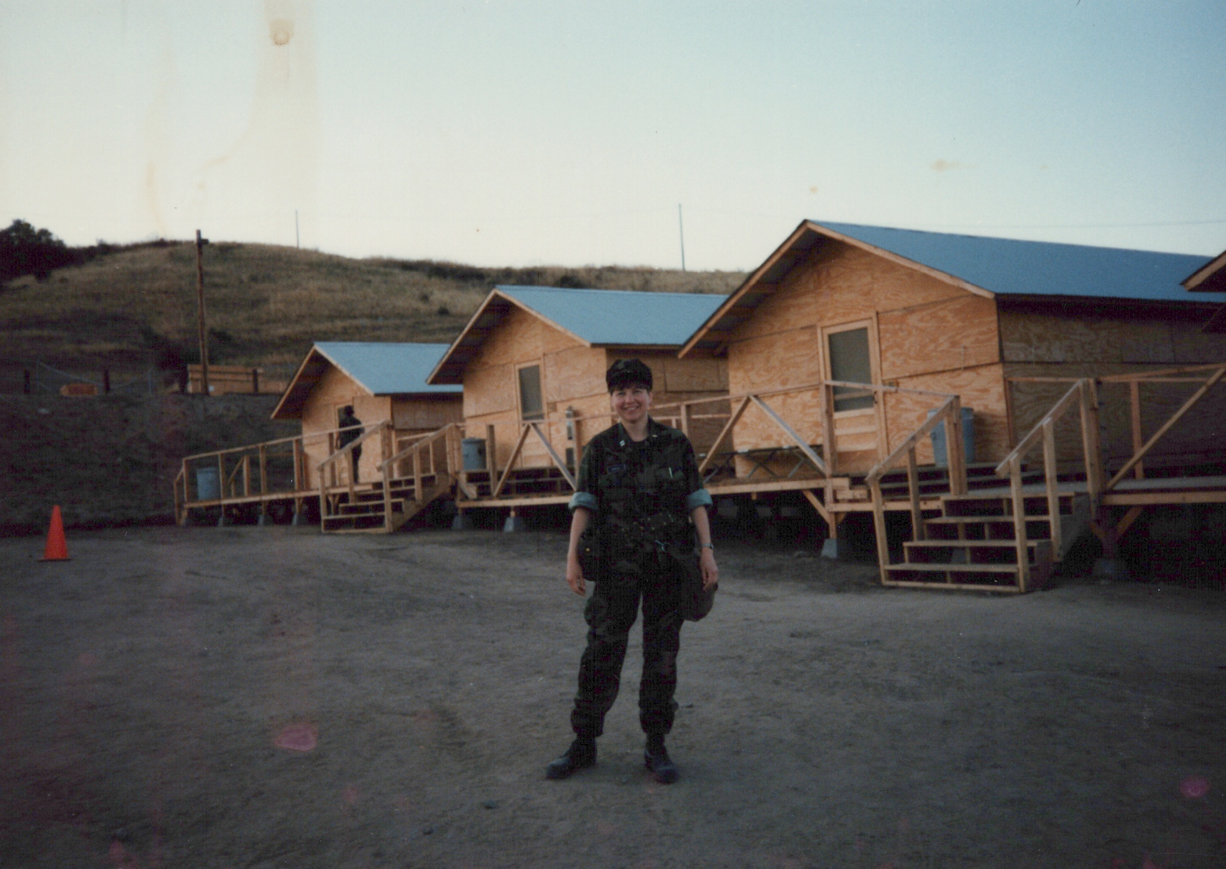 Fleet Hospital 007: Uniformed person in front of raised camp buildings.